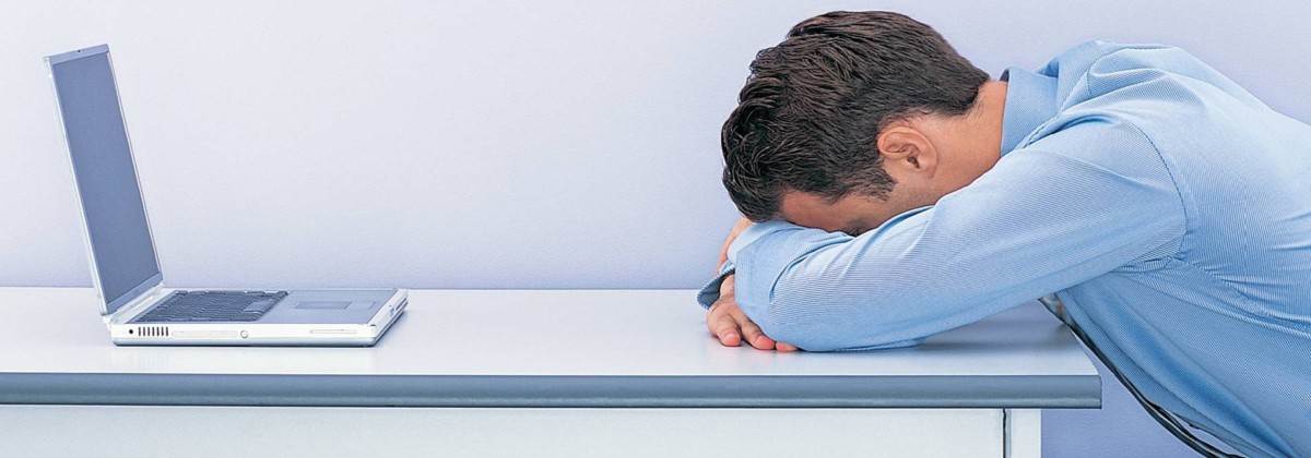 Frustrated man with head on desk next to WordPress website on laptop. Biggest mistake.